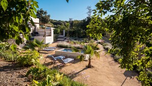 Um jardim com piscina, cadeiras de descanso e um edifício com pérgula.