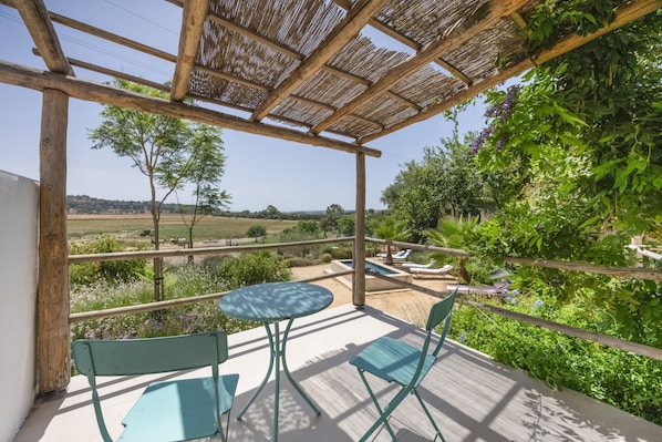 Un espace extérieur abrité, doté d’une table et de chaises, qui offre une vue sur un paysage arboré et une piscine.