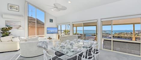 A modern dining area with a glass table and white chairs, overlooking a scenic ocean view.