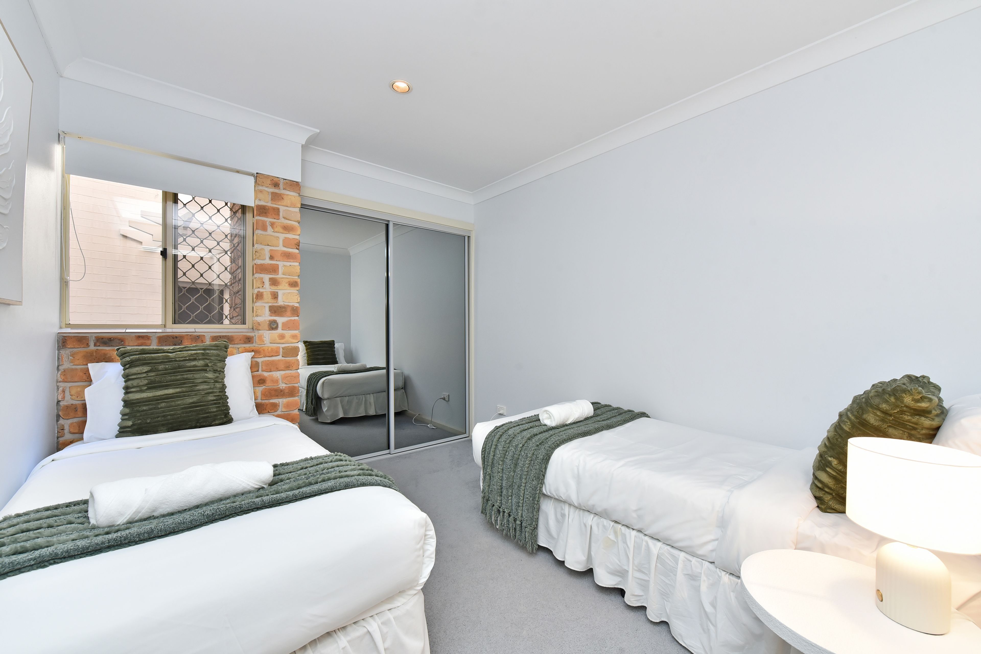 A hotel room with two beds, a large mirror, a small table, and a window with a view.