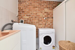 A laundry room with a brick wall, a washing machine, and a dryer. - Bella on Canomii Family Beach House in Nelson Bay (Nelson Bay)