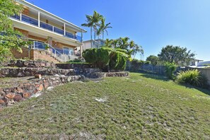 A residential property with a stone retaining wall, a grassy lawn, and a multi-story building with balconies. - Bella-Vista On Canomii (Nelson Bay)
