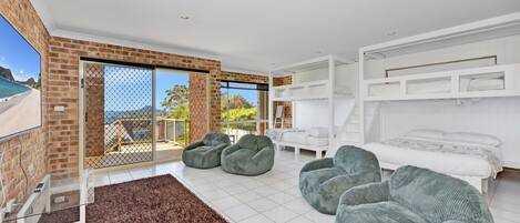 A modern living room with a large sliding glass door leading to a balcony, a white bed with a bunk bed above, and two green bean bag chairs.