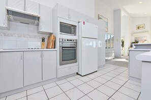 A modern kitchen with white cabinetry, a built-in oven, and a refrigerator. - Bella-Vista On Canomii (Nelson Bay)