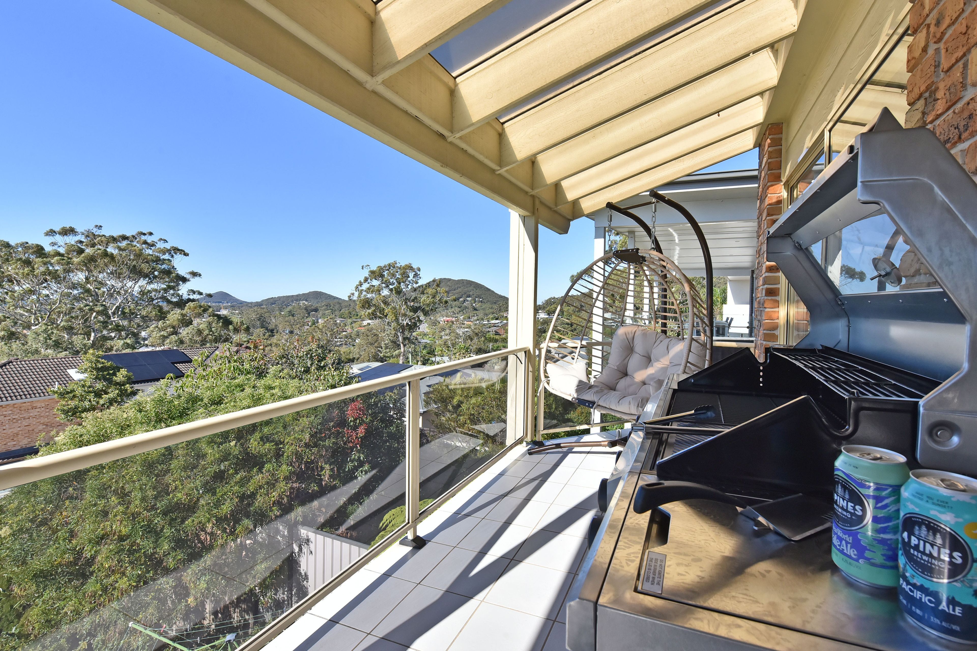 A balcony with a grill, a hanging chair, and two cans of beer.