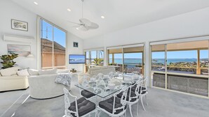 Un'ampia zona giorno con un tavolo da pranzo in vetro, posti a sedere confortevoli e una grande finestra vista mare.