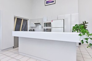 A modern kitchen with white cabinetry, a central island, a microwave, a refrigerator, and a potted plant. - Bella-Vista On Canomii (Nelson Bay)