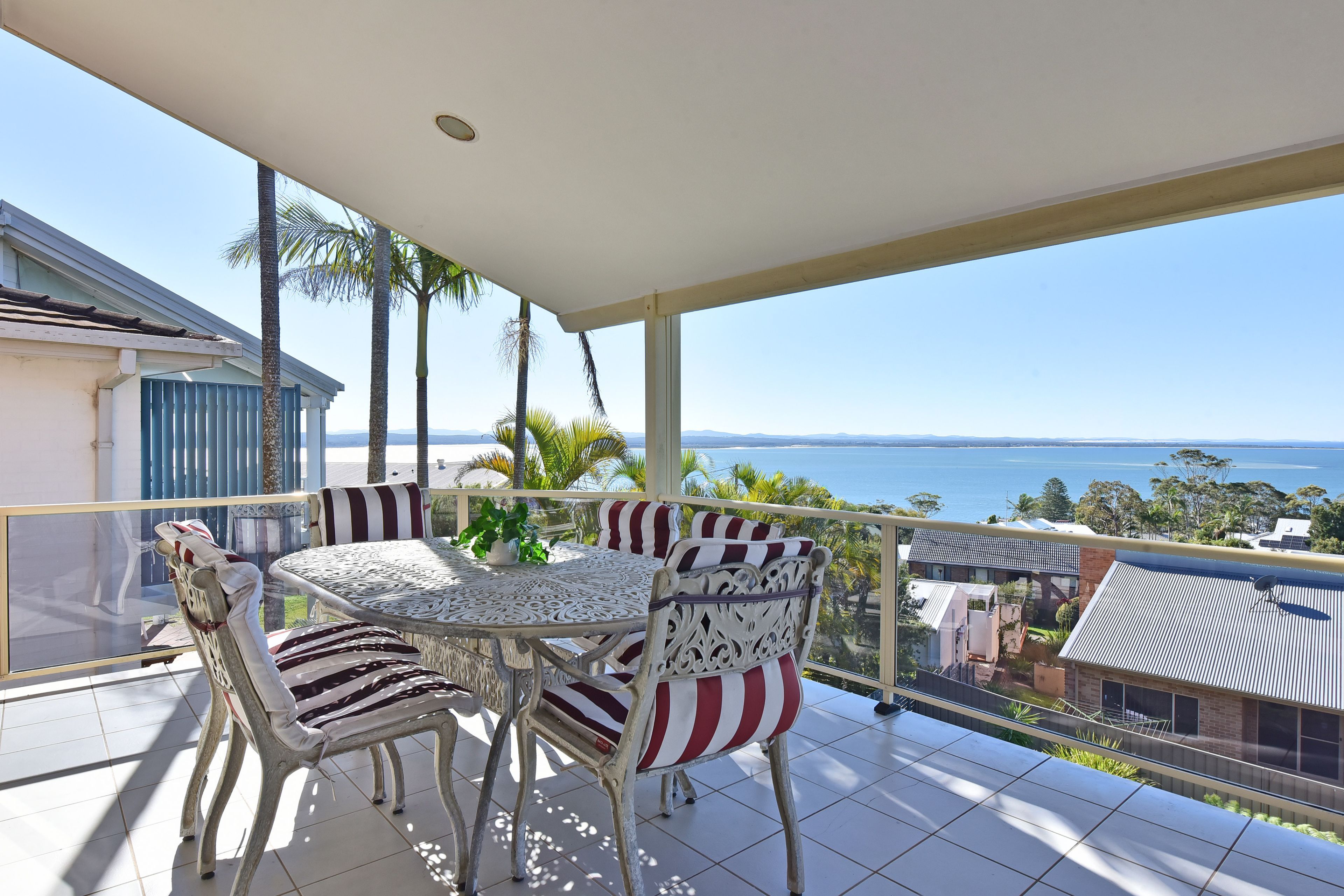 Ein Balkon mit Tisch und Stühlen, der auf ein Gewässer und entferntes Land blickt.