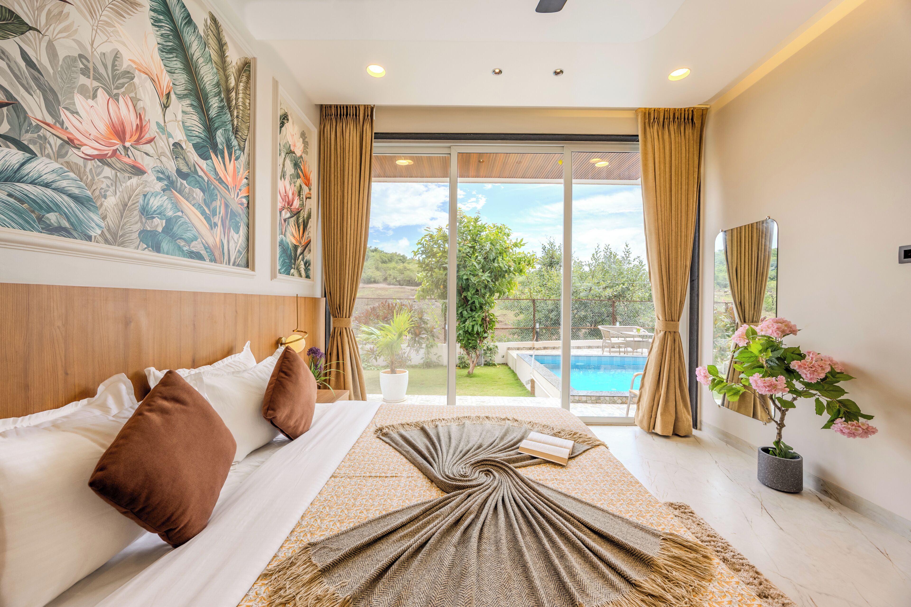 A bedroom with a bed, pillows, a large window with curtains, a view of a swimming pool, and a potted plant.