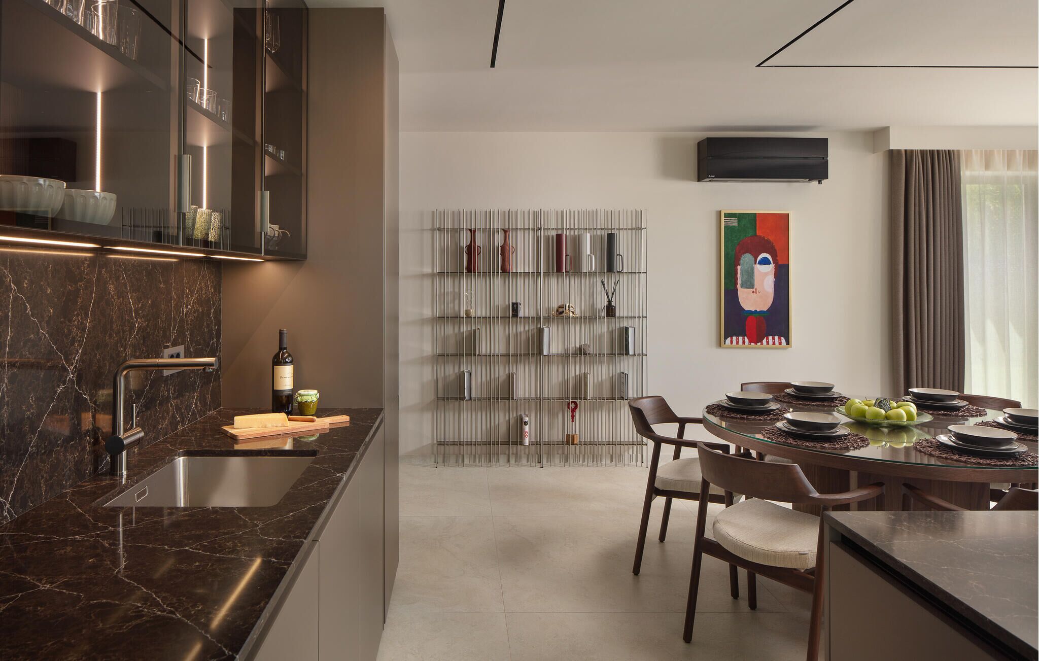 A modern kitchen with a marble countertop, a dining area with a glass table, and a wall-mounted air conditioner.