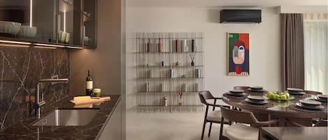 A modern kitchen with a marble countertop, a dining area with a glass table, and a wall-mounted air conditioner.