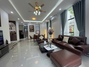 A modern living room with a brown leather sofa, a coffee table, and a ceiling fan. - Van Khe Cozy Villa (Hà Đông)