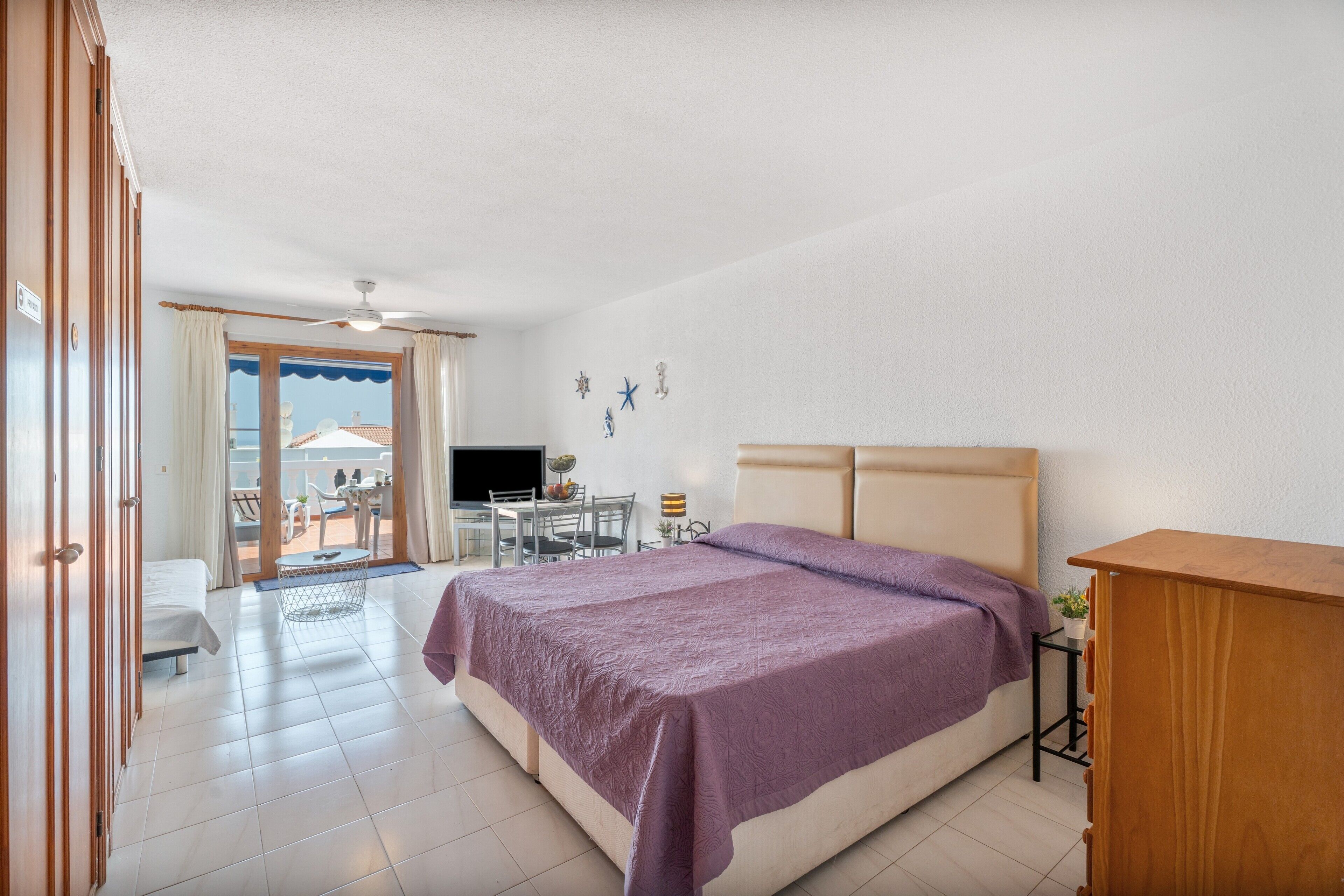 A hotel room with a bed, a desk, a chair, a television, and a balcony with a view.