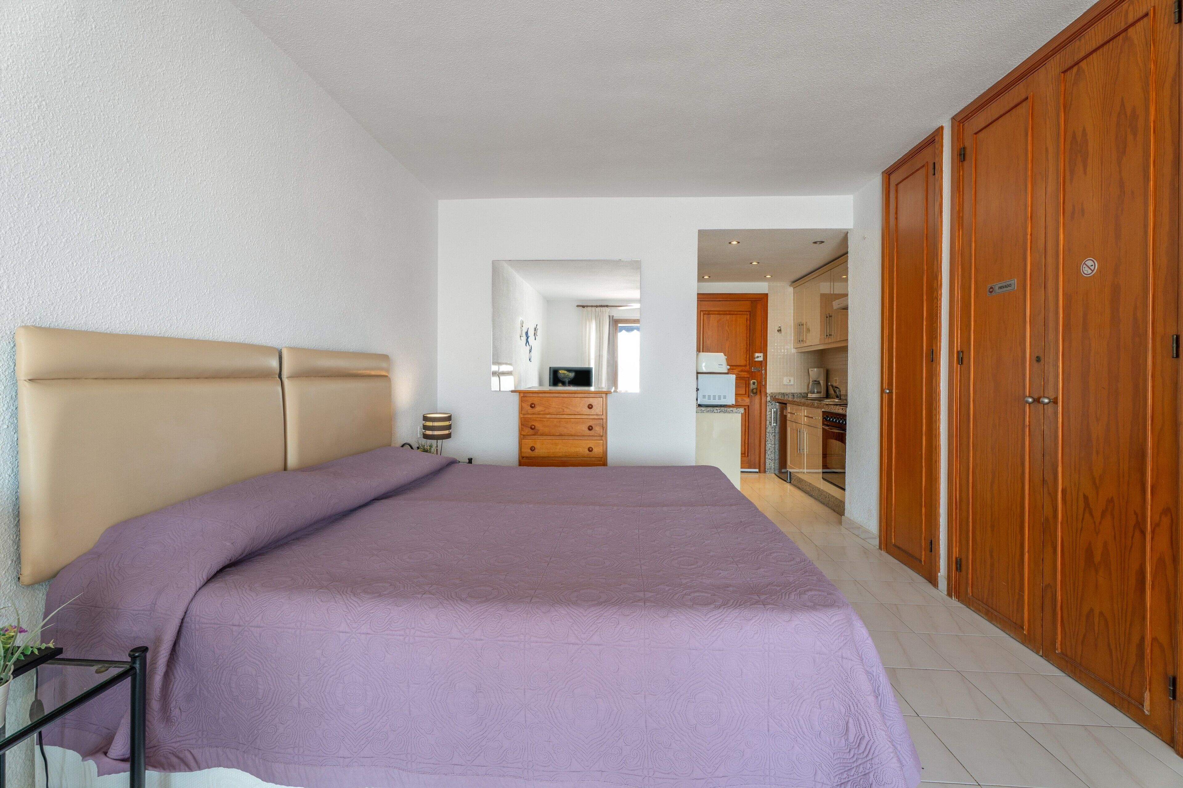 Een slaapkamer met een bed, een dressoir en uitzicht op de keuken.