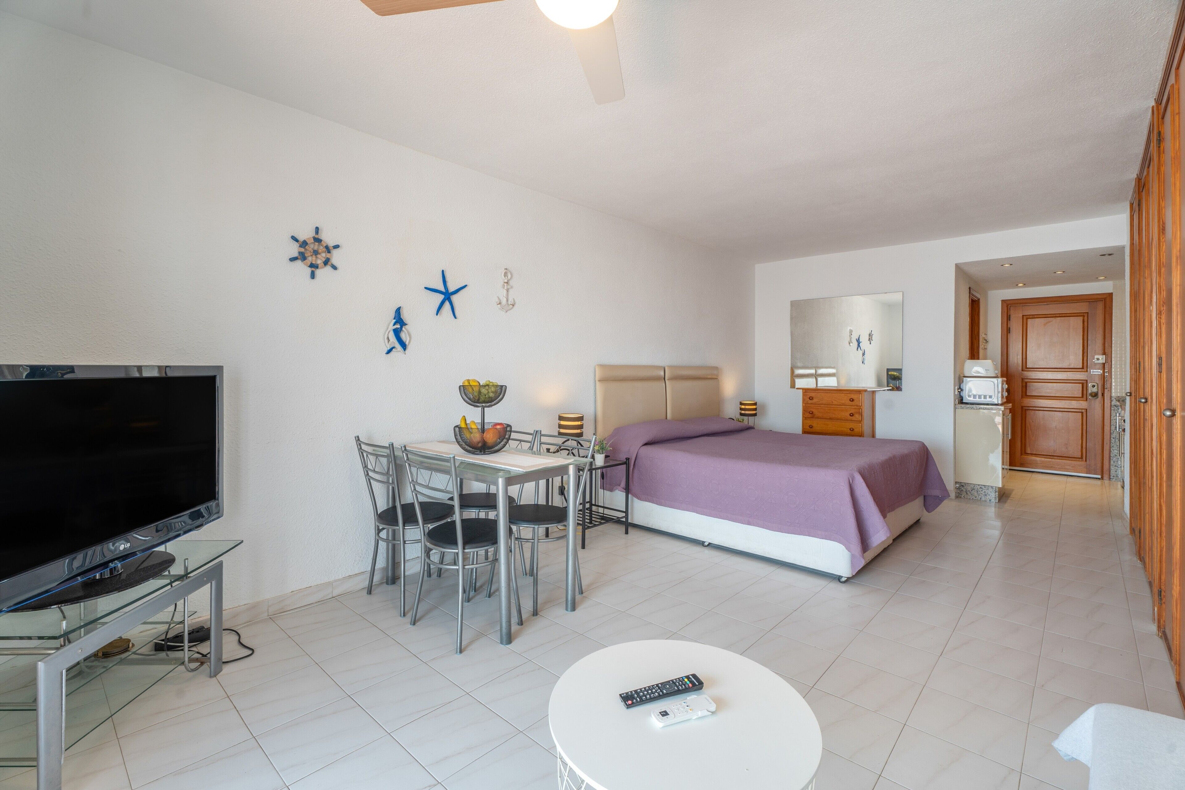 A hotel room with a bed, a desk with chairs, a television, and a small table with a remote control.