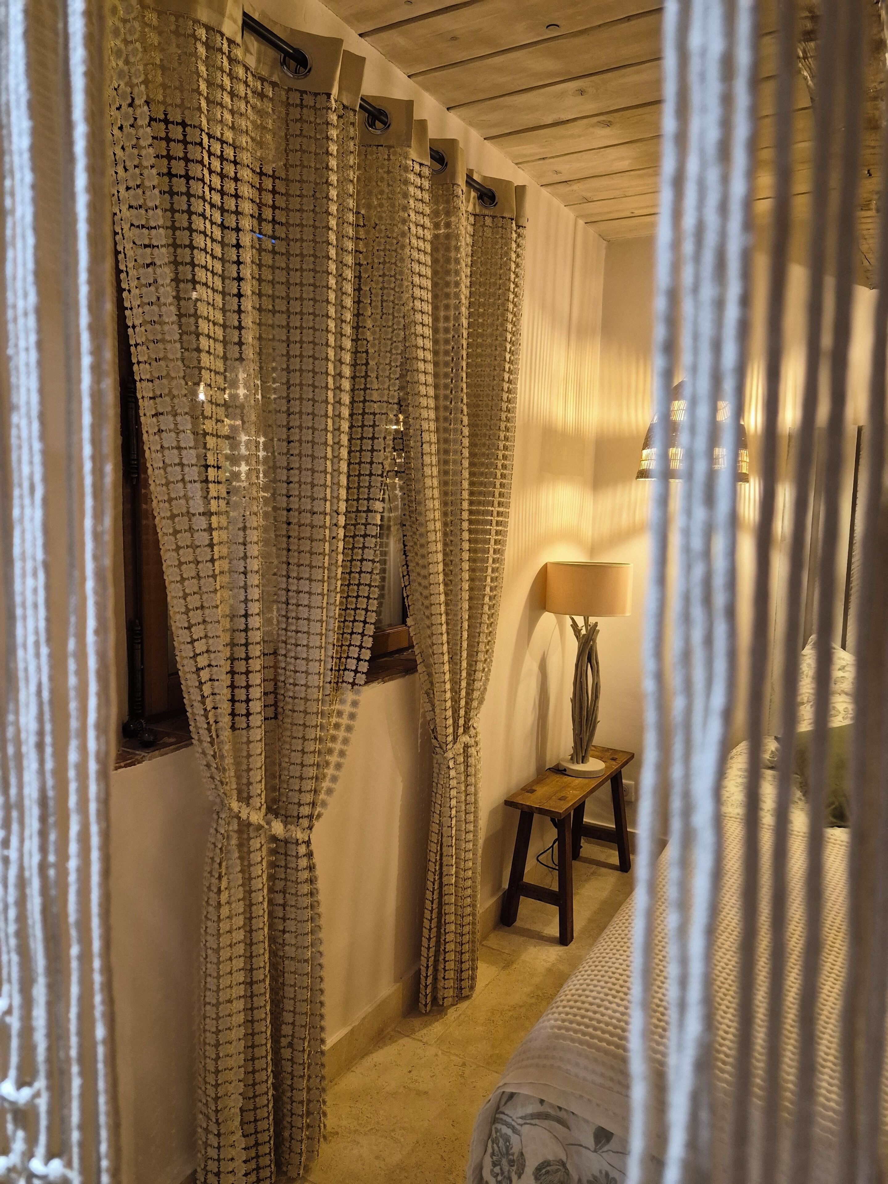 A room with a bed, a nightstand, a lamp, and a window with curtains.