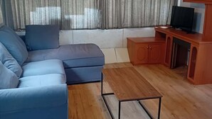 A living room with a sectional sofa, a wooden coffee table, a television on a stand, and a cabinet.