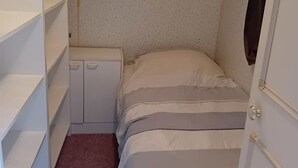 A small, narrow room with a bed, a desk, and a wardrobe.