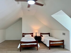 Una stanza con due letti di legno, una ventola a soffitto, una lampada a muro e un soffitto spiovente.