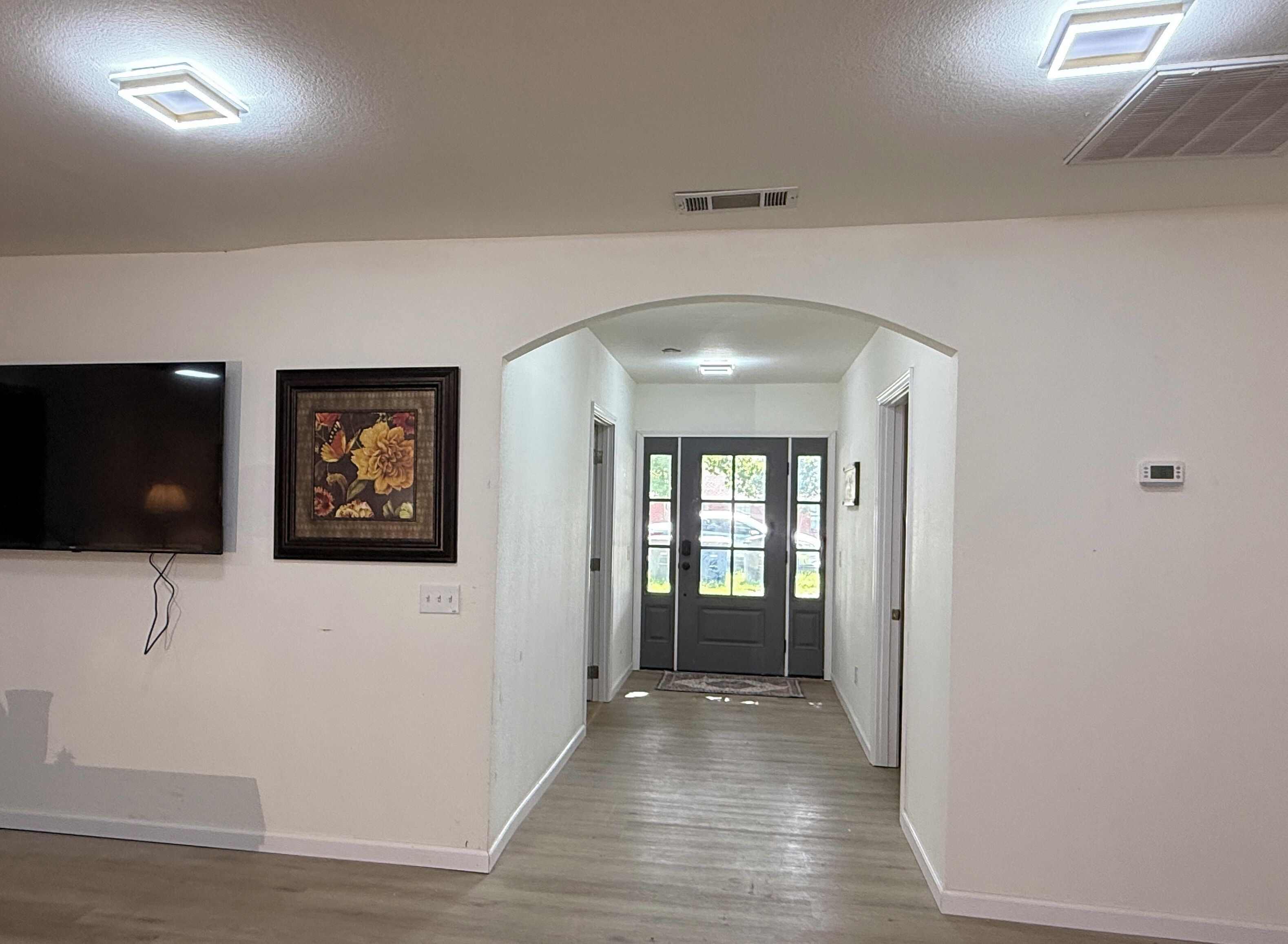 A hallway with a flat-screen TV mounted on the wall, a framed floral artwork, and a door leading to a car through a window.