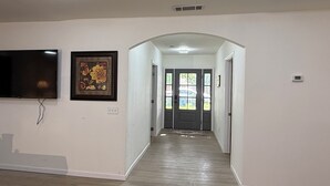 A hallway with a flat-screen TV mounted on the wall, a framed floral artwork, and a door leading to a car through a window.