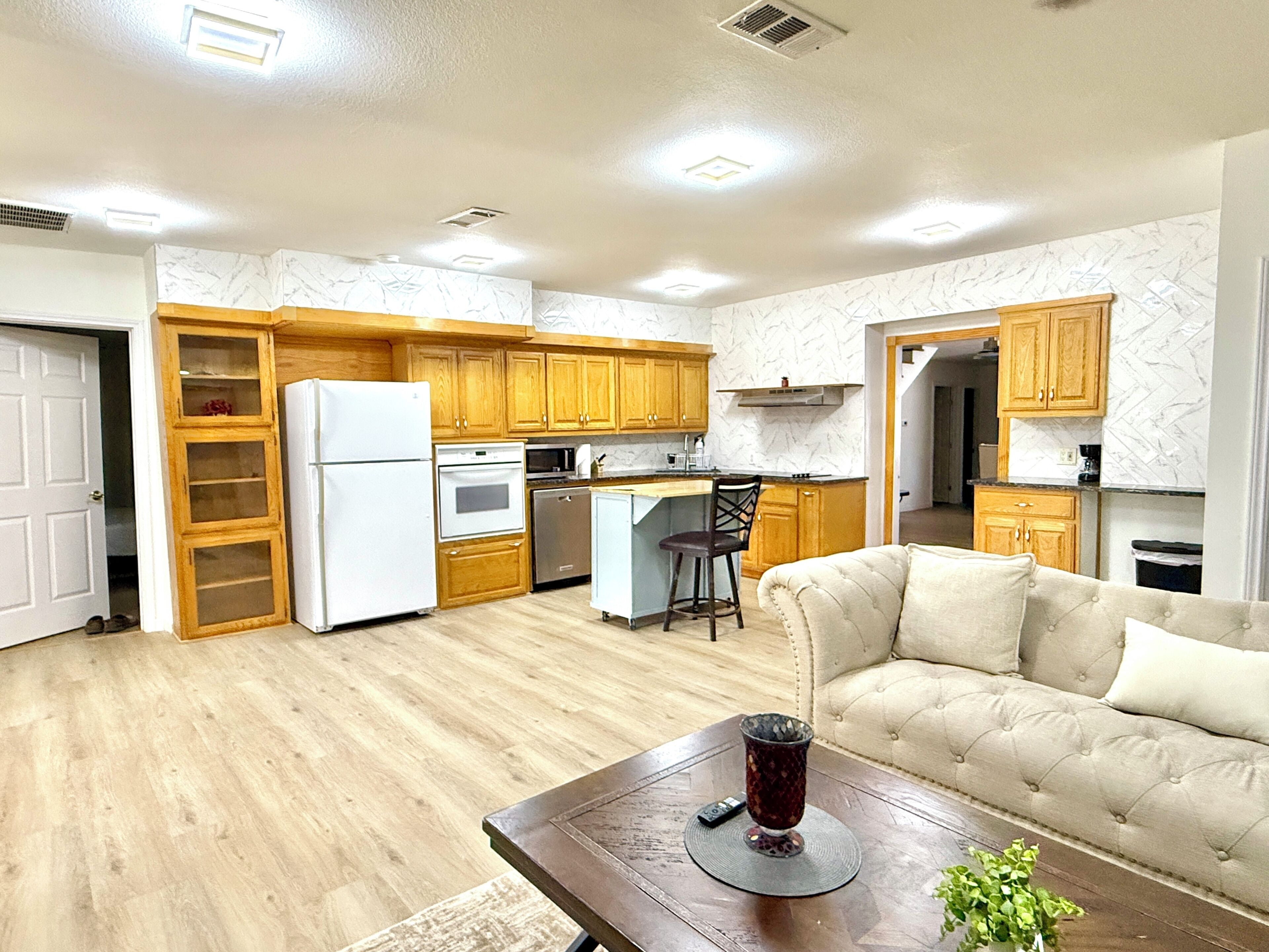 A modern kitchen with wooden cabinets, a refrigerator, and a dining area with a sofa and a coffee table.