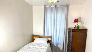 A bedroom with a bed, a dresser, a lamp, and a window with curtains.