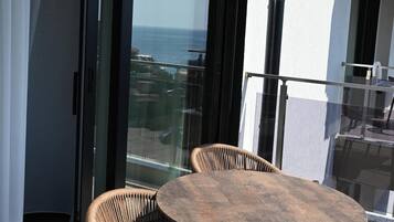 A balcony with a round table and two wicker chairs, overlooking a body of water.