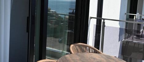A balcony with a round table and two wicker chairs, overlooking a body of water.