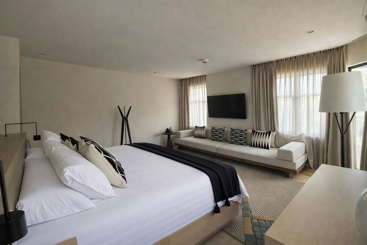 Quarto de hotel com uma cama grande, um sofá, uma TV e um abajur.