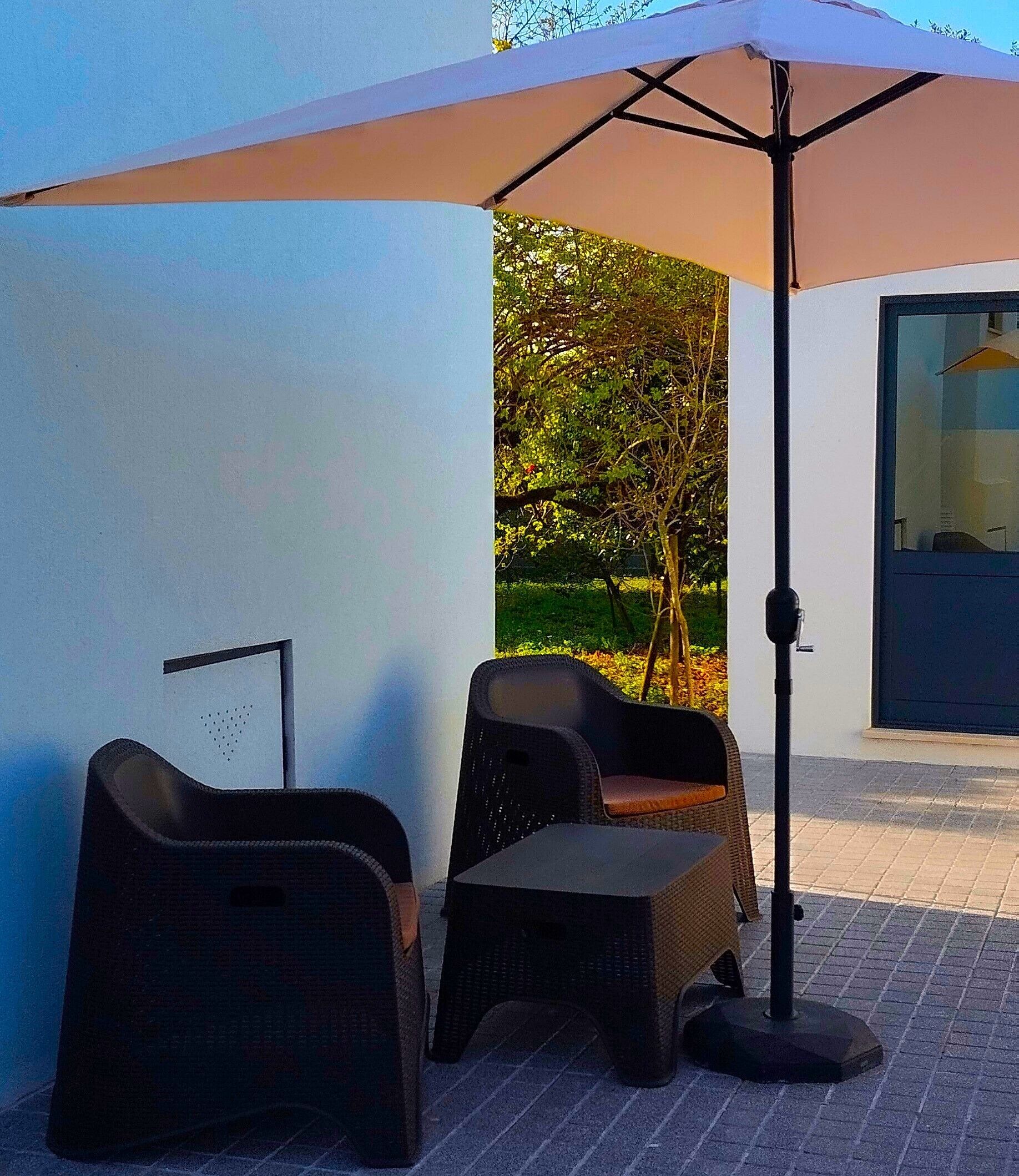 An outdoor seating area with two chairs and a table, a large umbrella, and a door to a building.