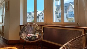 Ett rum med en hörnfönsterplats, en flätad stol och ett element.