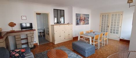 Ein Wohnzimmer mit einer Couch, einem Couchtisch, einem Fernseher, einem Esstisch mit Stühlen, einer Kommode und einem Bild an der Wand.