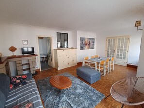 Ein Wohnzimmer mit einer Couch, einem Couchtisch, einem Fernseher, einem Esstisch mit Stühlen, einer Kommode und einem Bild an der Wand.
