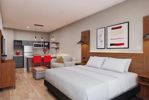 A modern hotel room with a large bed, a desk with a chair, a kitchenette, and artwork on the walls. - Hawthorn Extended Stay by Wyndham Brownsville (Los Fresnos)