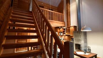 A wooden staircase leading to a lofted area with a stone fireplace and a hanging light fixture.