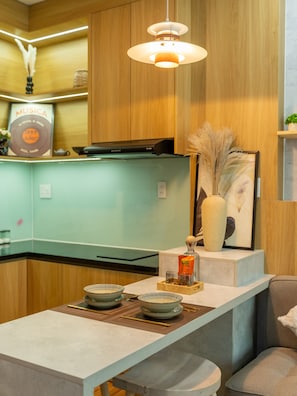 A modern kitchen with wooden cabinets, a light green countertop, and a hanging pendant light. - Babo Homestay 2 Da Nang (Da Nang)