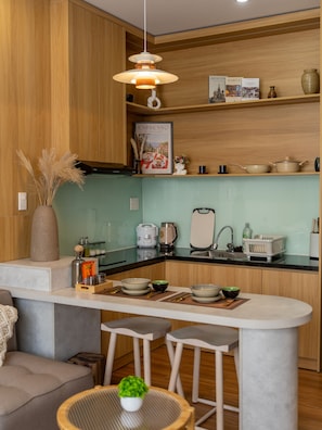 A modern kitchen with wooden cabinets, a central island with stools, a hanging light fixture, and a variety of kitchen appliances and utensils. - Babo Homestay 2 Da Nang (Da Nang)