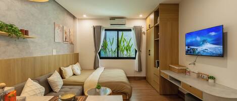 A modern hotel room with a bed, sofa, dining table, and a TV.