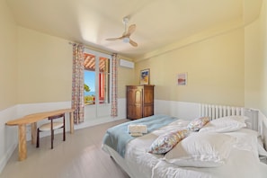 Un dormitorio con cama, escritorio de madera, silla, armario y ventilador de techo.