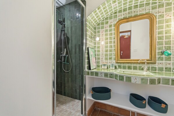 A bathroom with a shower, a sink with a mirror, and a shelf with baskets. - Villa Arcadia: Sleeps 14, 5x11 Pool, Ocean View, Near the Beach, Petanque, Ping-Pong (Carqueiranne)