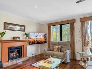 A living room with a fireplace, a sofa, a coffee table, and a TV mounted on the wall. - Villa Magenta - 2-Storey Villa at Cypress Lakes Resort (POKOLBIN)
