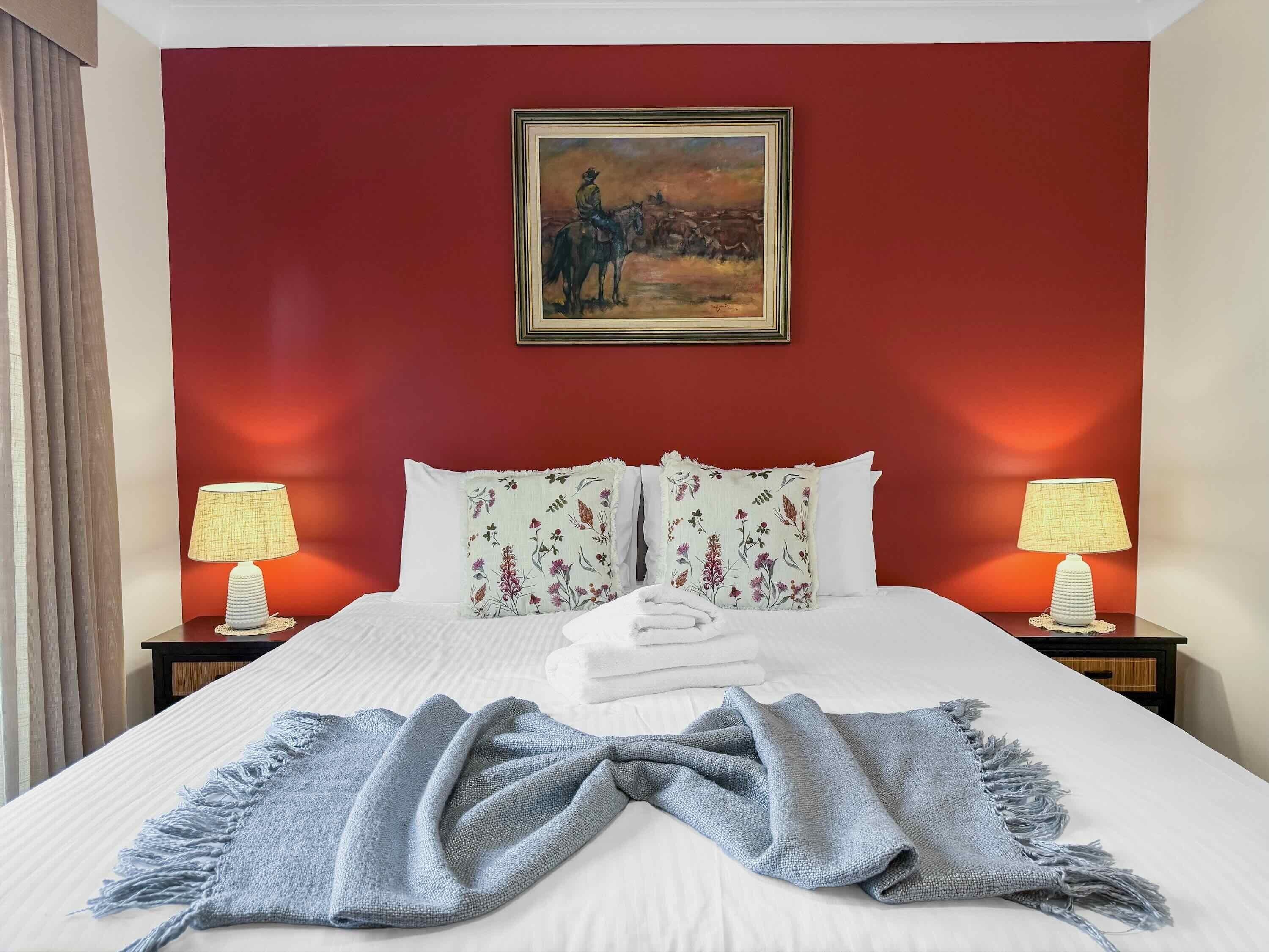 Una camera d'albergo con un letto, due lampade ai comodini, un quadro appeso e una finestra con tende.