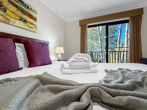 A hotel room with a bed, a painting on the wall, a window with a view of trees, and a balcony. - Villa Magenta - 2-Storey Villa at Cypress Lakes Resort (POKOLBIN)