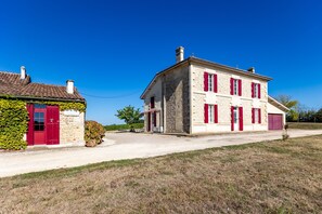 A two-story stone building with red shutters and a red door, adjacent to a smaller building with a red door and ivy-covered wall. - Château Haut Cazevert Guesthouse with Pool, Wi-Fi, and Air Conditioning (Blasimon)