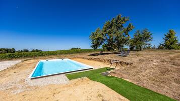 A rectangular swimming pool with a clear blue water surface, surrounded by a sandy area and a patch of green artificial turf.