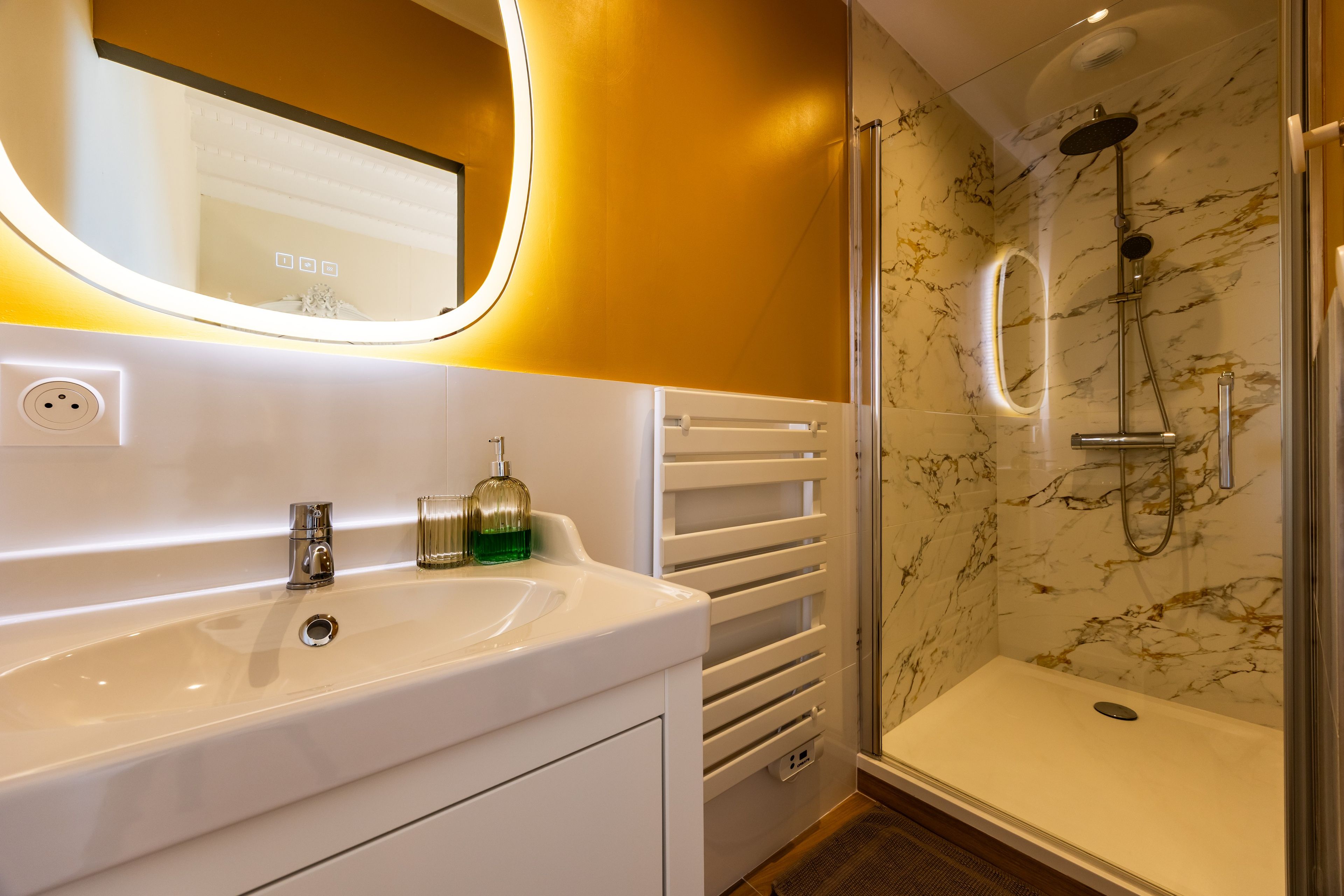 A bathroom with a white sink, a mirror, a shower with a glass door, and marble walls.