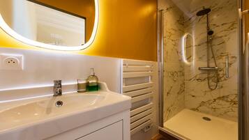 A bathroom with a white sink, a mirror, a shower with a glass door, and marble walls.