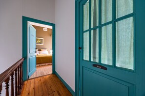 A hallway leading to a bedroom with a bed, a nightstand, and a wall-mounted lamp. - Château Haut Cazevert Guesthouse with Pool, Wi-Fi, and Air Conditioning (Blasimon)