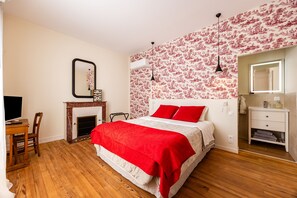 A bedroom with a bed, a desk, a chair, a fireplace, and a bathroom with a mirror and sink. - Château Haut Cazevert Guesthouse with Private Pool, Wi-Fi, and Air Conditioning (Blasimon)